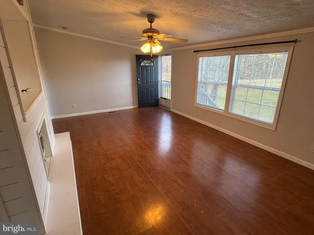 a view of an empty room with wooden floor and fan