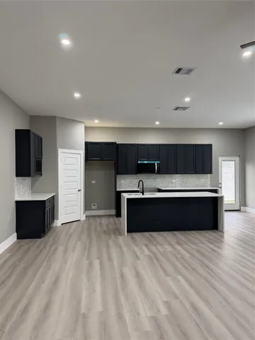 a living room with stainless steel appliances furniture wooden floor and a kitchen view