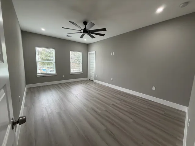 an empty room with wooden floor fan and windows