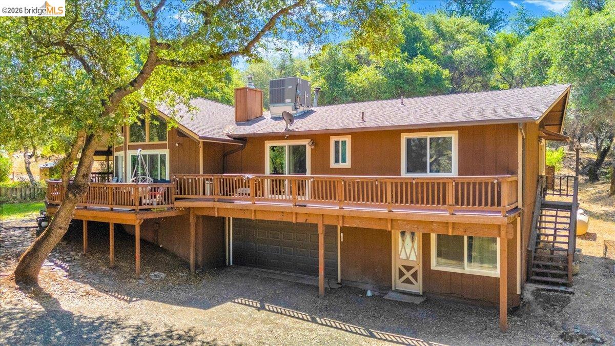 8733 Fraguero Road Sonora, CA 95370 - Photo 5 of 73 Spacious elevated wood-sided residence featuring a large wood deck with railing, a two-story window array, a chimney, and an attached garage with a dark door
