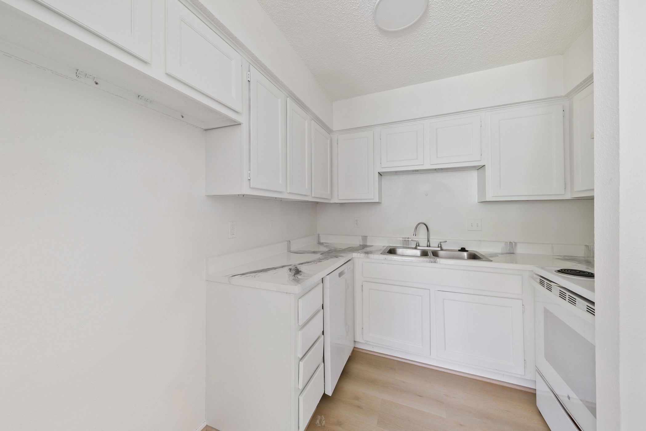700 Lyle W Avenue, Unit D Cleveland, TX 77327 - Photo 4 of 16 This compact kitchen features an all-white design with ample cabinetry, a dual sink, and modern appliances, creating a clean and bright space.