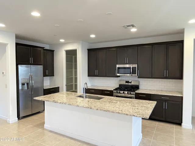 a kitchen with granite countertop stainless steel appliances a stove a sink a refrigerator a counter top space and cabinets