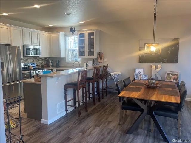 a kitchen with stainless steel appliances granite countertop a stove a refrigerator a sink a dining table and chairs with wooden floor