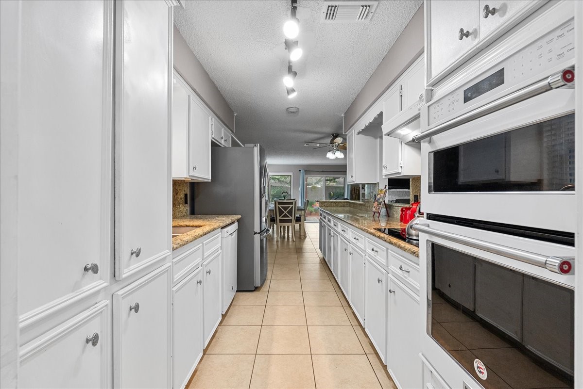 883 Silverpines Road Houston, TX 77062 - Photo 15 of 38 This kitchen features a galley layout with ample white cabinetry, modern appliances, and granite countertops. The space is brightened by overhead lighting and opens to a dining area with natural light from large windows.