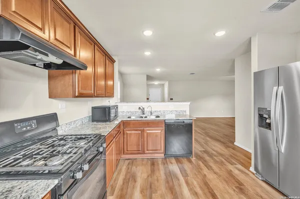 a kitchen with stainless steel appliances granite countertop a stove top oven a sink dishwasher and a refrigerator with wooden floor