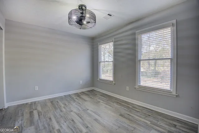 an empty room with wooden floor fan and windows