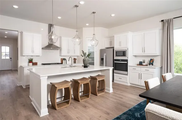 a large kitchen with stainless steel appliances kitchen island granite countertop a stove a sink a refrigerator and white cabinets with wooden floor