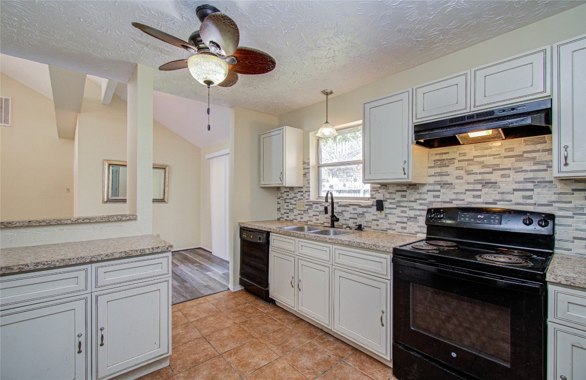 4911 Tealgate Drive Spring, TX 77373 - Photo 18 of 41 This kitchen features modern amenities with granite countertops, a tile backsplash, and an electric stove. It includes light cabinetry, a double sink, and a ceiling fan, offering a cozy and functional space with a view into the adjoining room.