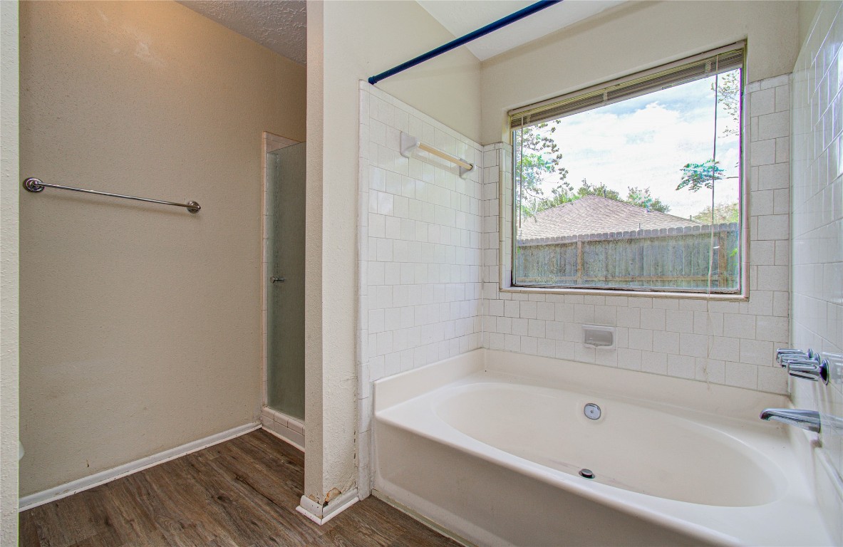 4911 Tealgate Drive Spring, TX 77373 - Photo 26 of 41 Cozy bathroom featuring a spacious bathtub with tiled surround and a large window offering natural light. The room includes a separate shower area and wood-style flooring.