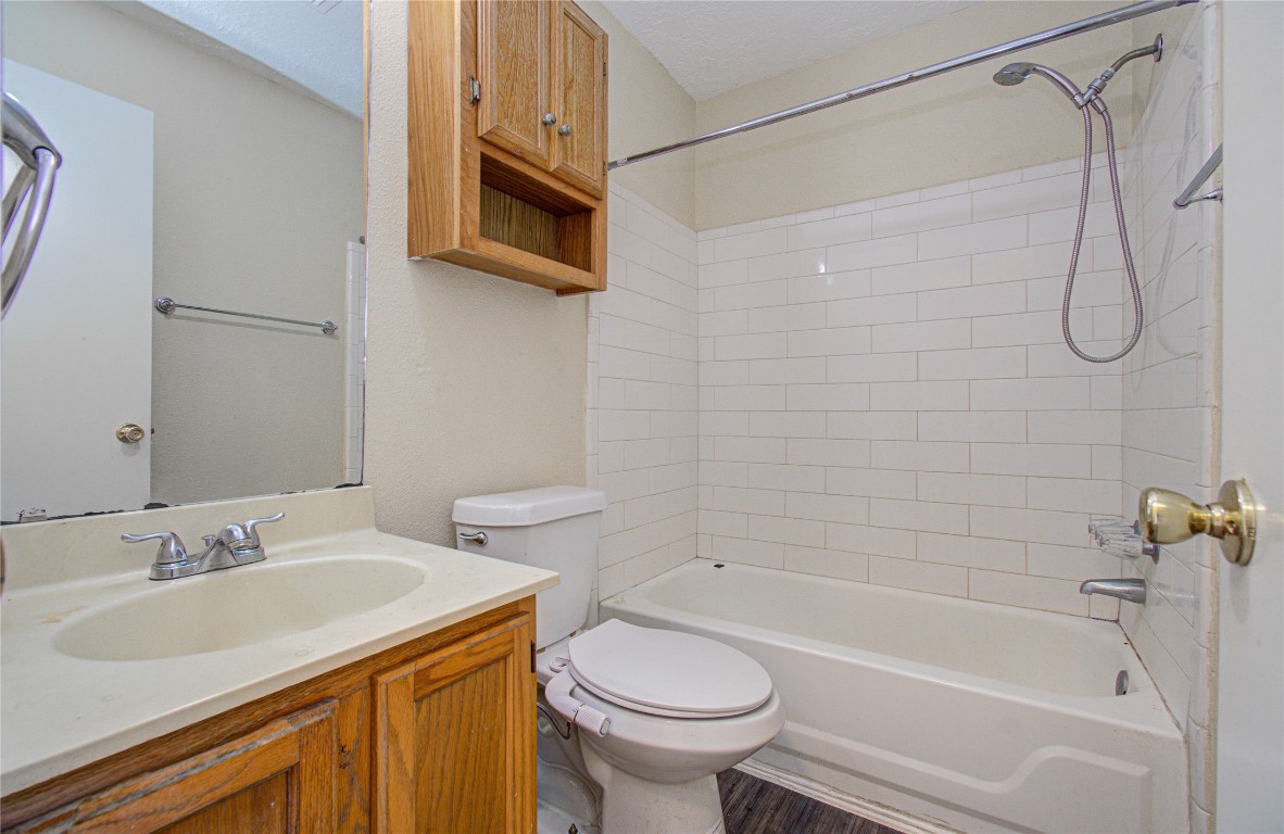 4911 Tealgate Drive Spring, TX 77373 - Photo 28 of 41 This bathroom features a classic design with a white tiled shower-tub combo, a wooden cabinet above the toilet, and a vanity with a light-colored countertop. The flooring complements the neutral tones, creating a clean and functional space.