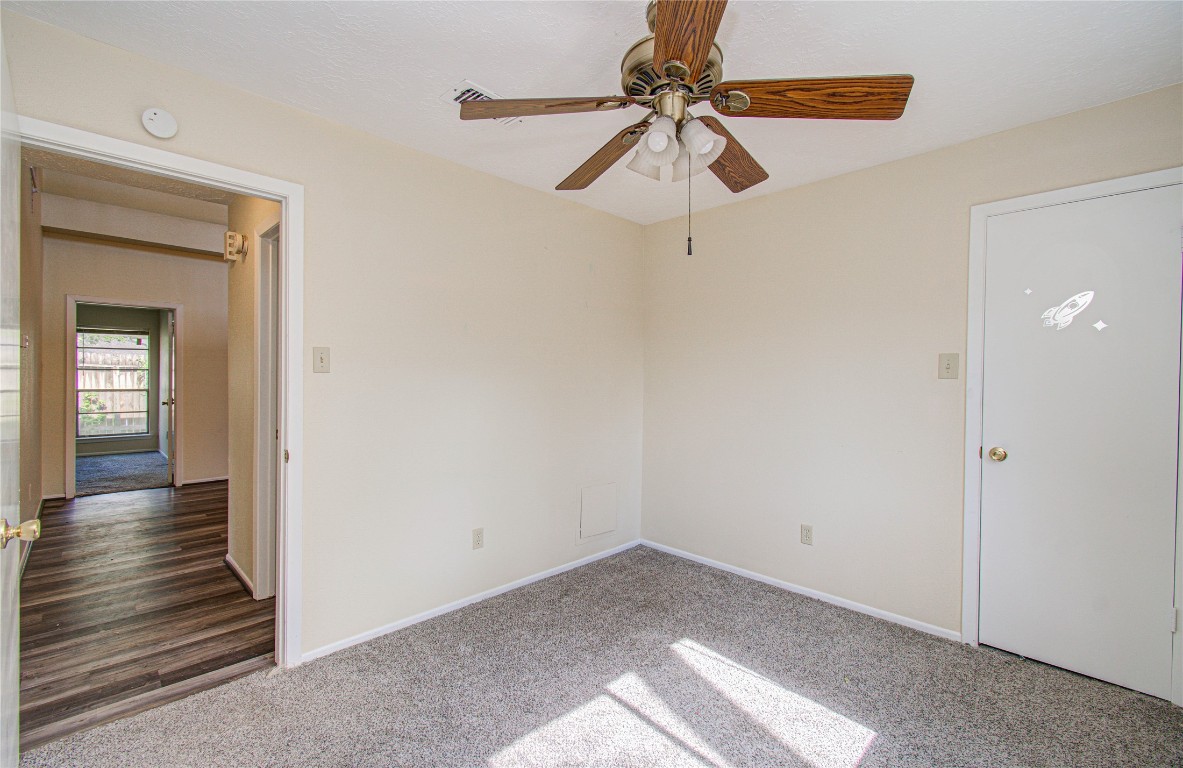 4911 Tealgate Drive Spring, TX 77373 - Photo 30 of 41 This room features neutral walls, carpeted flooring, and a ceiling fan. It has a door leading to a hallway with wood-style flooring and visible natural light from an adjacent room.