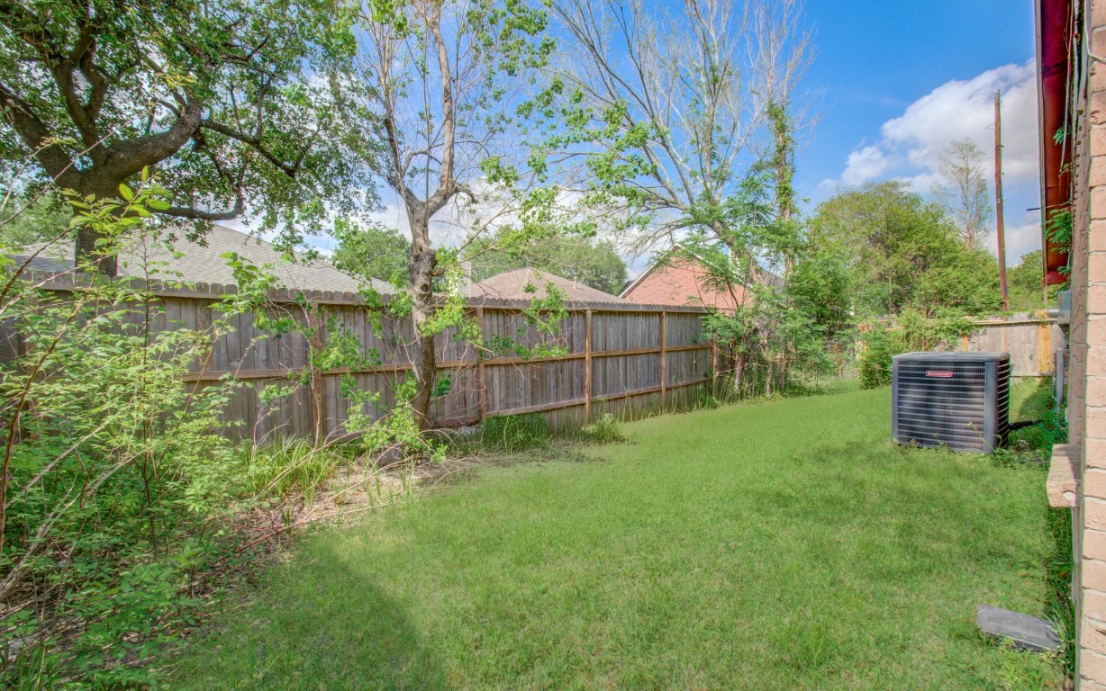 4911 Tealgate Drive Spring, TX 77373 - Photo 38 of 41 This photo shows a quaint backyard with a grassy area, bordered by a wooden fence and shaded by mature trees. There's an air conditioning unit next to the house, providing a practical feature for comfortable living.
