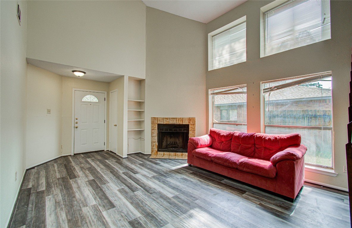 4911 Tealgate Drive Spring, TX 77373 - Photo 7 of 41 Bright living room with high ceilings, featuring large windows, a cozy fireplace, and modern flooring. Includes a red sofa and built-in shelving for added storage.
