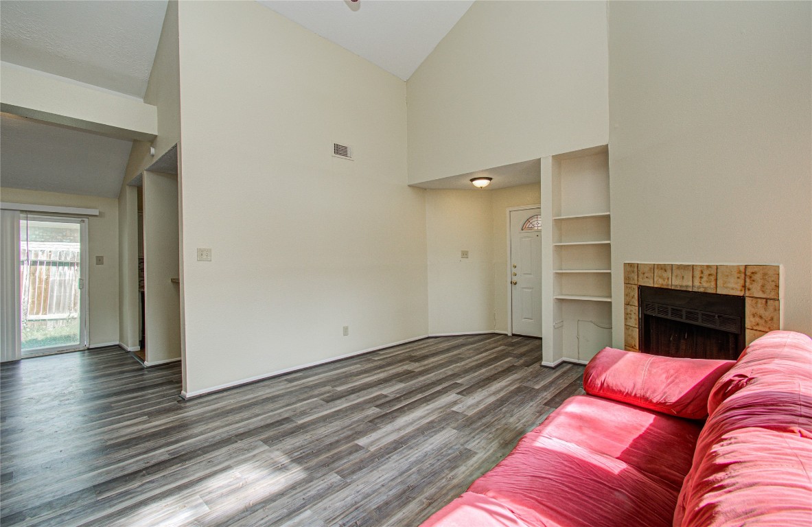4911 Tealgate Drive Spring, TX 77373 - Photo 8 of 41 This living room features high ceilings, neutral walls, and wood-style flooring. It includes a cozy fireplace, built-in shelving, and a sliding glass door leading to the backyard, enhancing natural light and space.