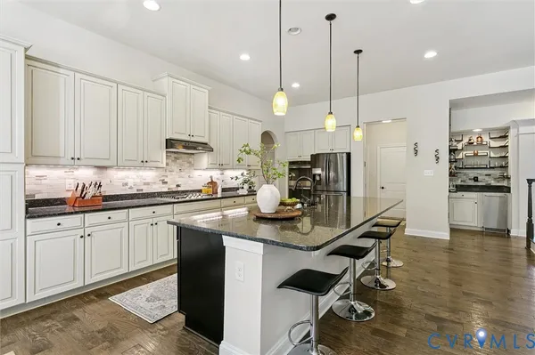 a kitchen with stainless steel appliances granite countertop a sink a stove a refrigerator and chairs
