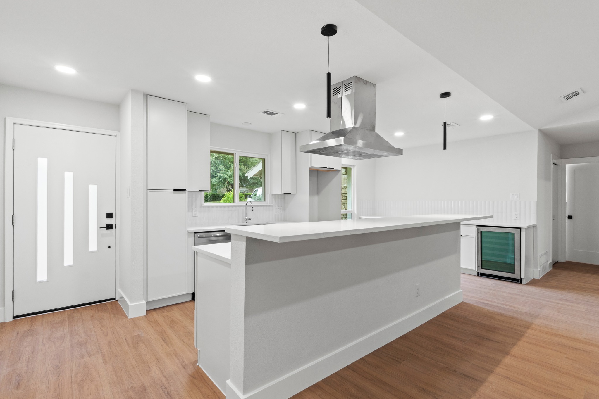 1608 Springer Lane Austin, TX 78758 - Photo 27 of 35 Contemporary kitchen featuring a large island with a solid surface countertop, stainless steel range hood, built-in beverage refrigerator, recessed lighting, and wood-finish flooring
