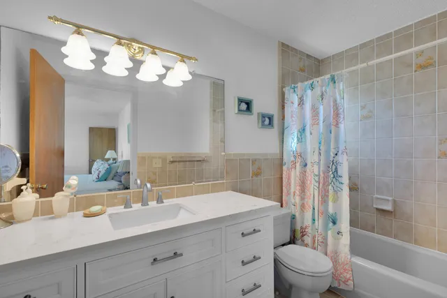 a bathroom with a granite countertop sink a toilet a mirror a vanity a bathtub and shower