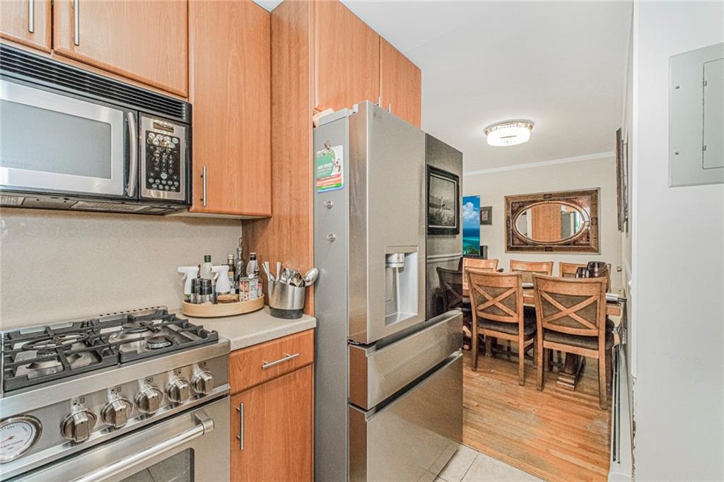 2809 East 28th Street, Unit 1C Brooklyn, NY 11235 - Photo 19 of 38 a kitchen with stainless steel appliances granite countertop a stove top oven a refrigerator a dining table and chairs with wooden floor