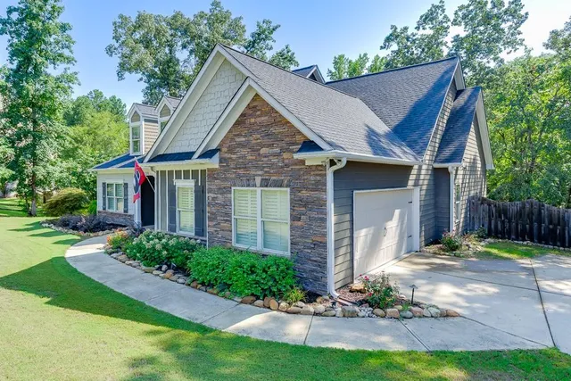 a view of a brick house with a yard plants and a large tree