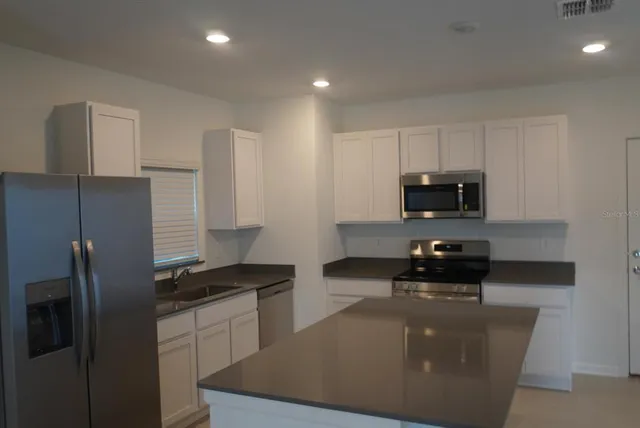 a kitchen with stainless steel appliances a sink a stove a microwave a refrigerator a stove and cabinets