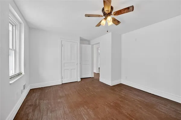 an empty room with wooden floor fan and windows