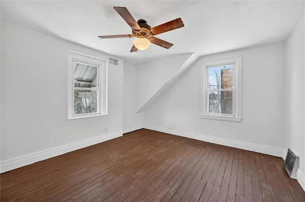 a view of an empty room with wooden floor and a ceiling fan
