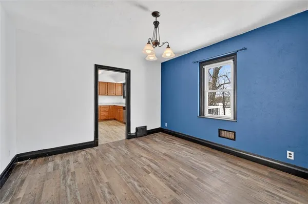an empty room with wooden floor chandelier and windows