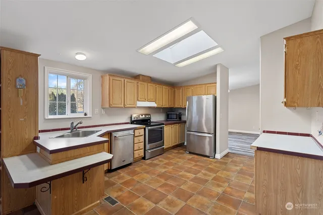 a large kitchen with a stove a sink dishwasher a refrigerator and wooden cabinets
