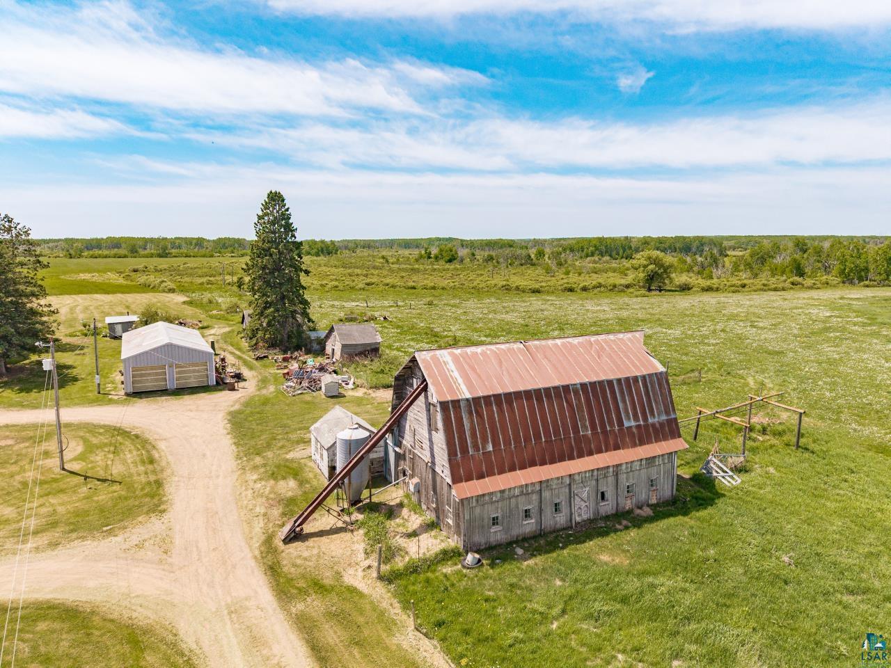 6606 Metso Road Kettle River, MN 55757 - Photo 39 of 84 Expansive rural property featuring a large barn with a rust-colored metal roof, a substantial metal outbuilding, a tall evergreen tree, and vast open fields