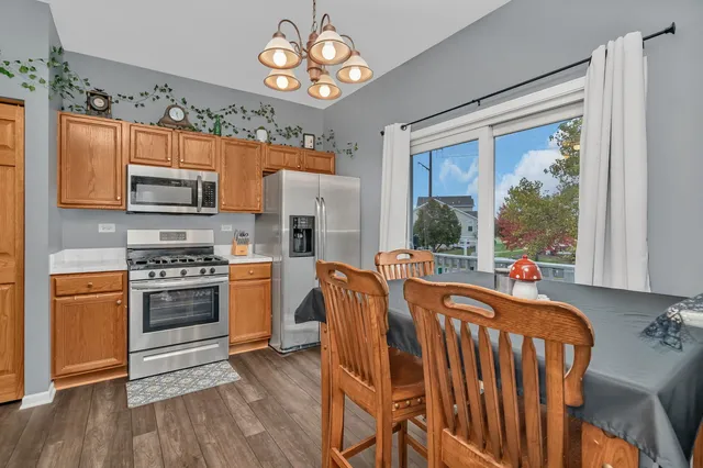 a kitchen with stainless steel appliances granite countertop a stove top oven a refrigerator and a dining table with wooden floor