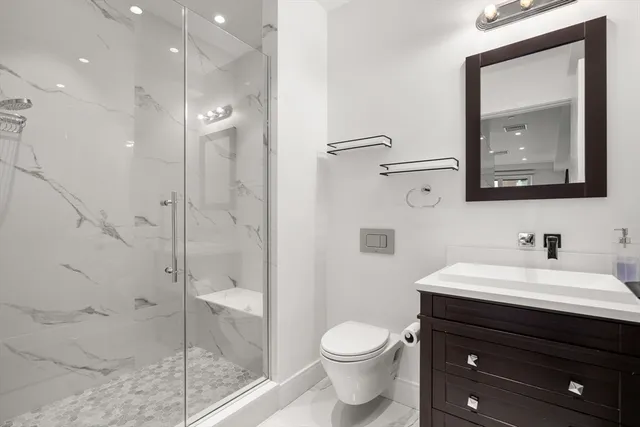 a bathroom with a toilet a sink a glass door a shower a mirror and vanity