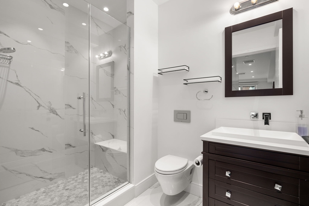 69 Walnut Street, Unit 4/5 Brookline, MA 02445 - Photo 13 of 26 a bathroom with a toilet a sink a glass door a shower a mirror and vanity