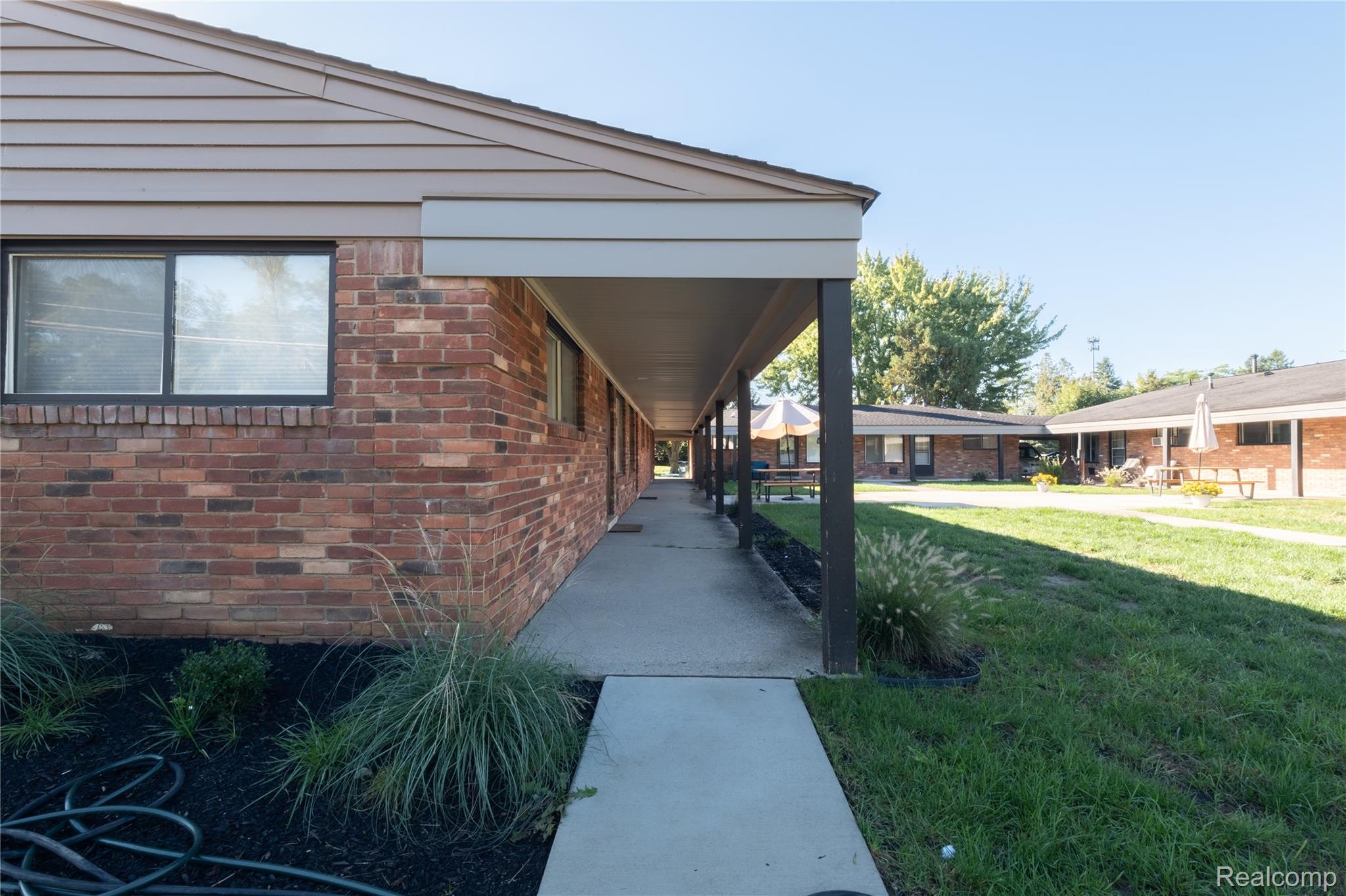 3065 South Commerce Road, Unit 9 Walled Lake, MI 48390 - Photo 13 of 15 Brick exterior with horizontal siding, covered walkway, concrete path, and planted landscaping
