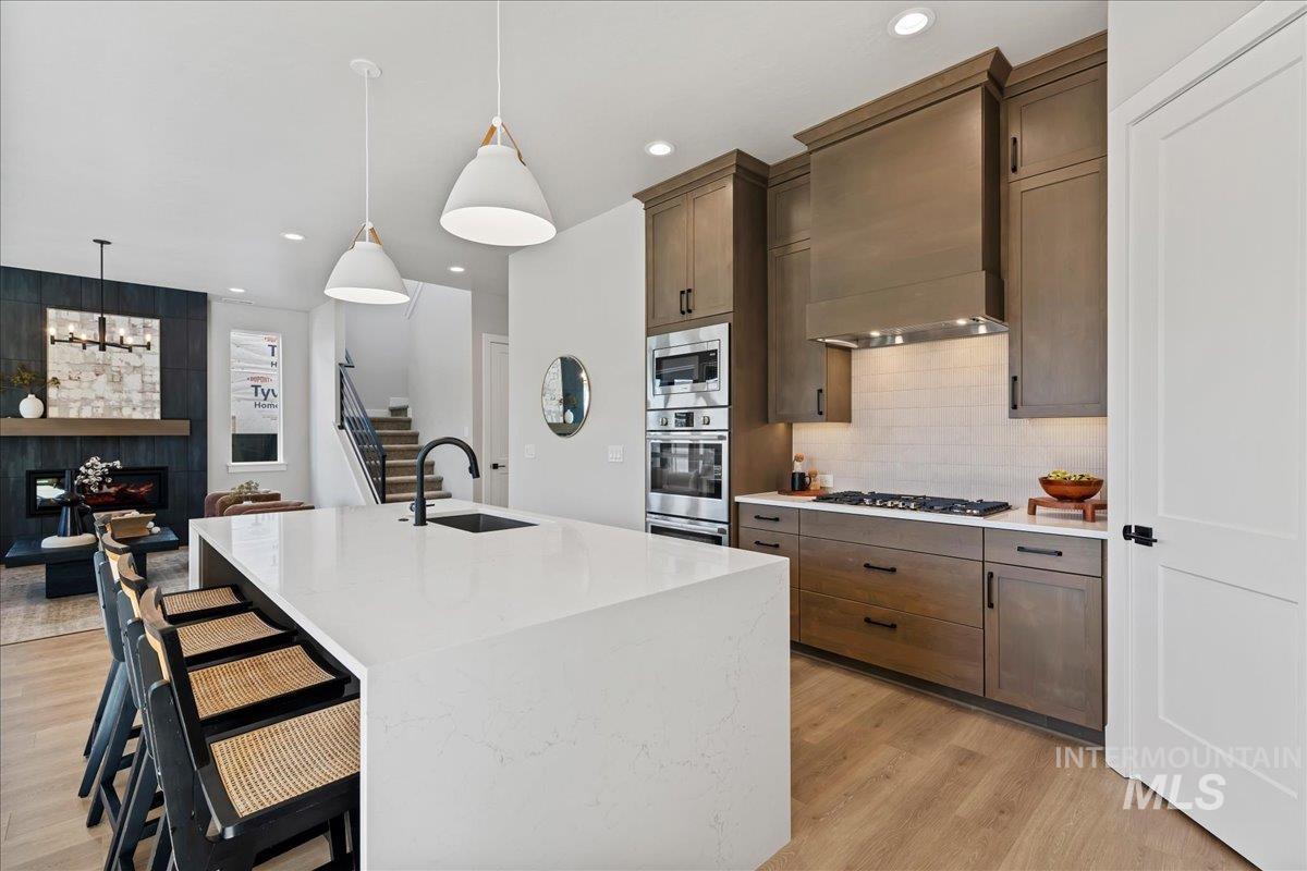 985 West Malbar Street Meridian, ID 83646 - Photo 12 of 39 Open-concept kitchen featuring a waterfall island with integrated sink, wood-finish flooring, recessed lighting, and stainless steel appliances
