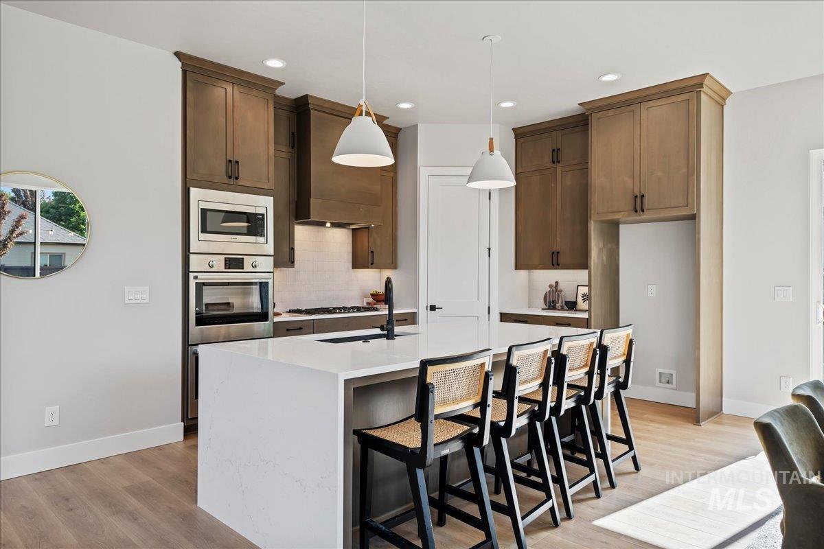 985 West Malbar Street Meridian, ID 83646 - Photo 14 of 39 Modern kitchen featuring a large center island with seating, stainless steel appliances, wood-finish cabinetry, white subway tile backsplash, and recessed lighting