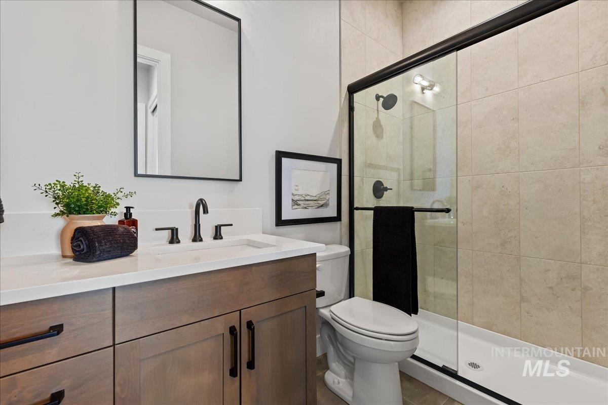985 West Malbar Street Meridian, ID 83646 - Photo 28 of 39 Bathroom featuring a walk-in shower with glass enclosure, beige tiled walls, a wood-finish vanity with a white countertop and integrated sink, and matte black fixtures