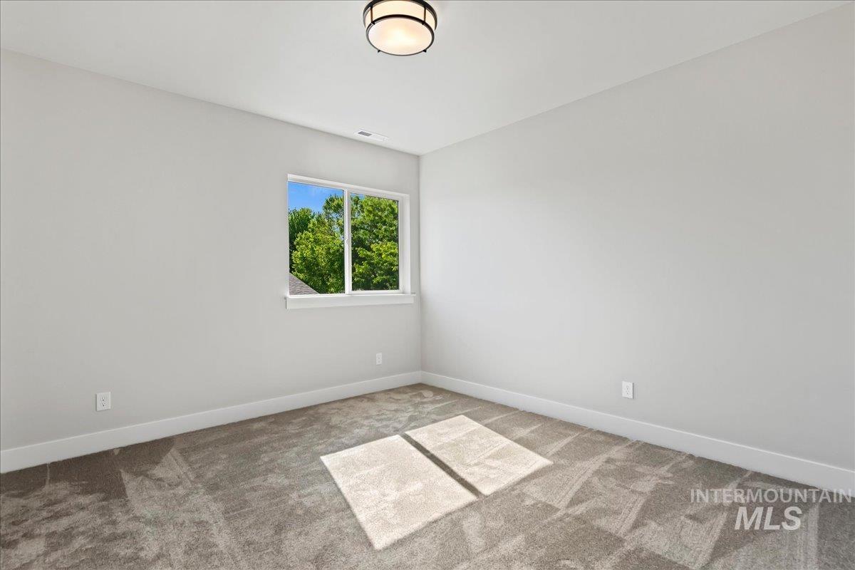 985 West Malbar Street Meridian, ID 83646 - Photo 30 of 39 Neutral-toned room featuring a window with exterior greenery, a flush-mount ceiling light fixture, and grey patterned carpeting