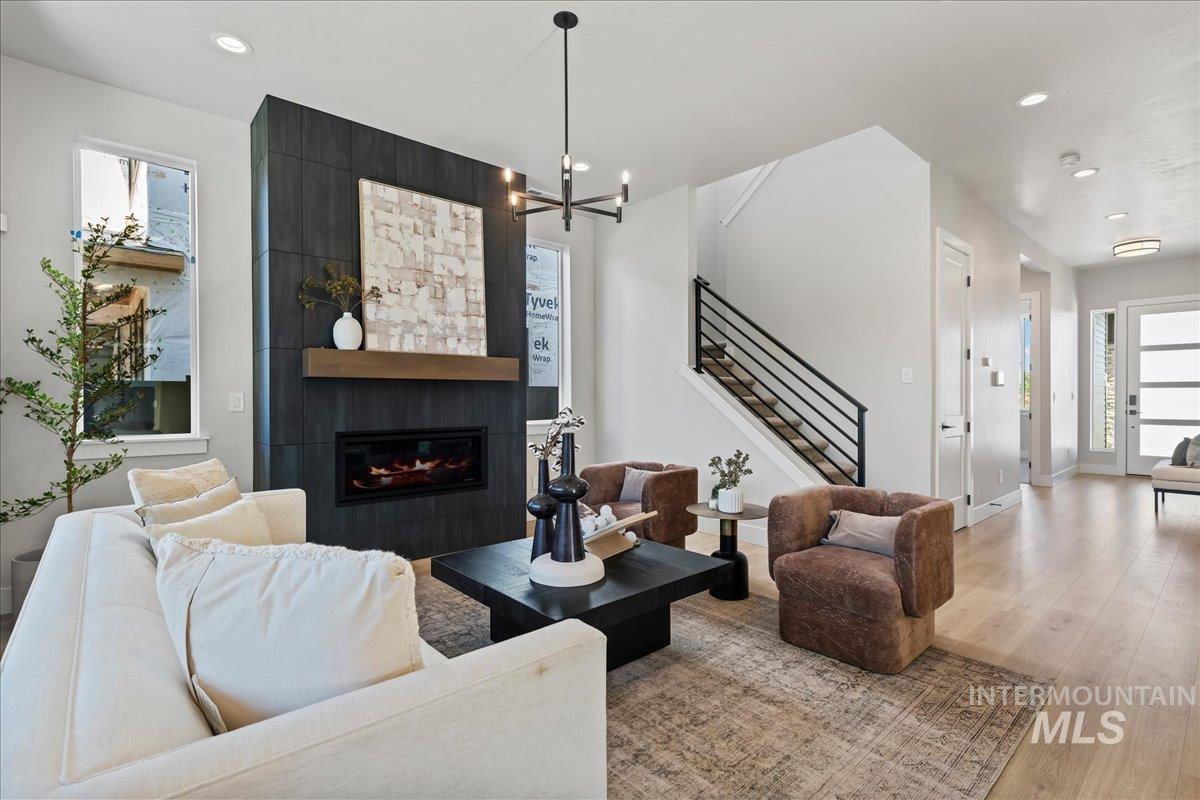 985 West Malbar Street Meridian, ID 83646 - Photo 6 of 39 Spacious living area featuring a floor-to-ceiling dark tile fireplace with a wood mantle, light wood-finish flooring, and a contemporary open-riser staircase with metal railings