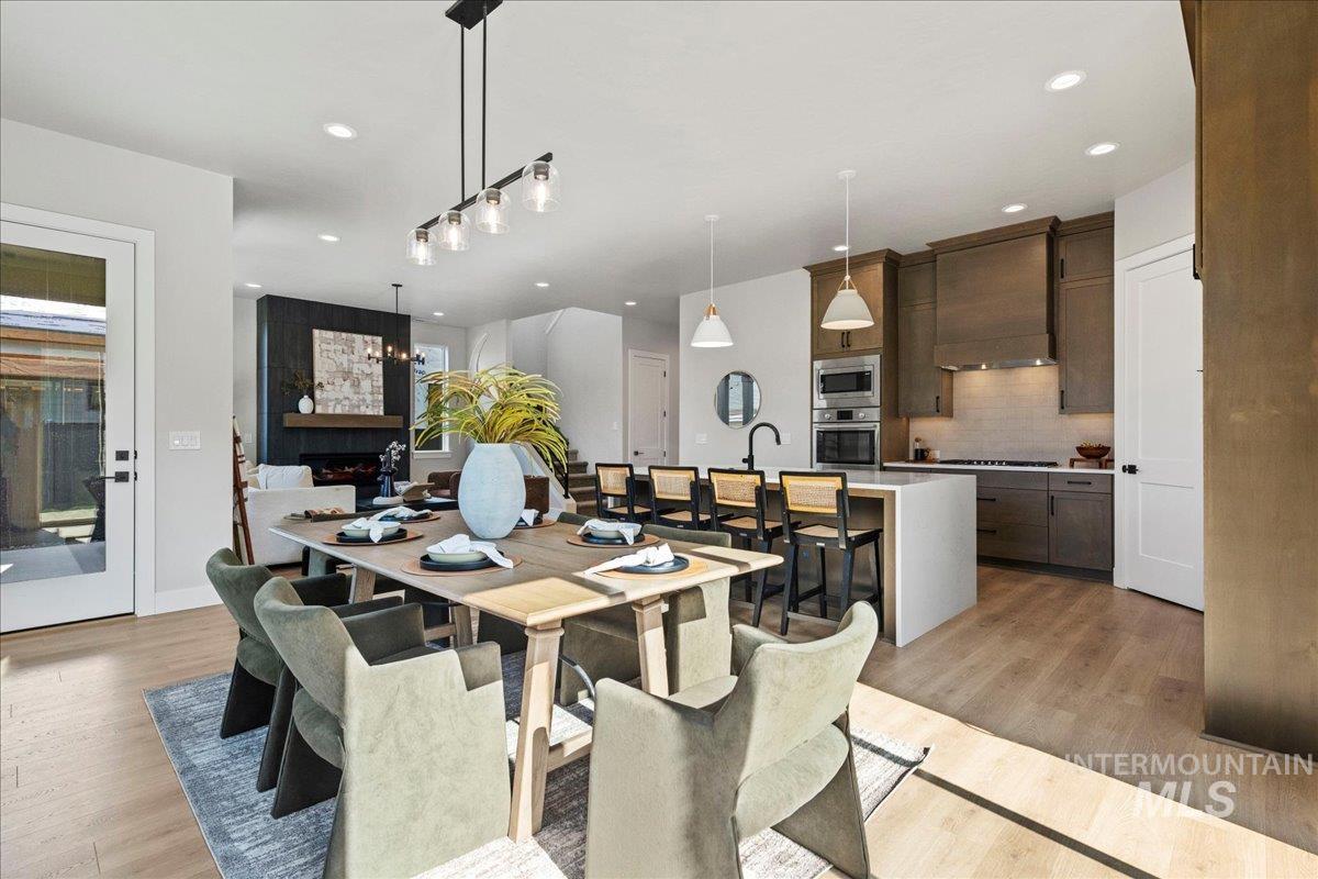 985 West Malbar Street Meridian, ID 83646 - Photo 10 of 39 Open-concept living space featuring wood-finish flooring, a contemporary kitchen with light cabinetry and built-in appliances, a central island with bar seating, and a fireplace with dark paneling