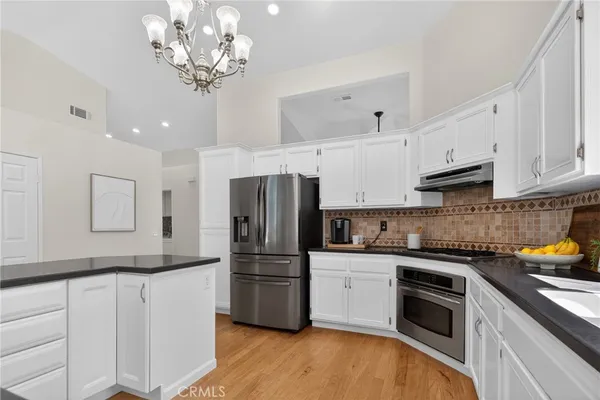 a kitchen with stainless steel appliances granite countertop a refrigerator a sink dishwasher a stove and white cabinets with wooden floor