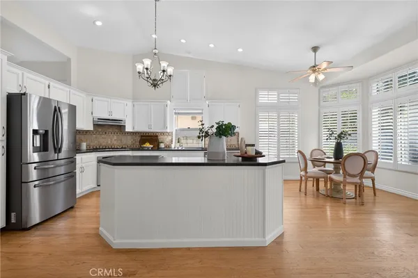 a kitchen with stainless steel appliances granite countertop a refrigerator a stove top oven a sink dishwasher a dining table and chairs with wooden floor