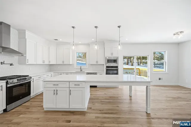 a large kitchen with granite countertop a stove a sink and white cabinets with wooden floor