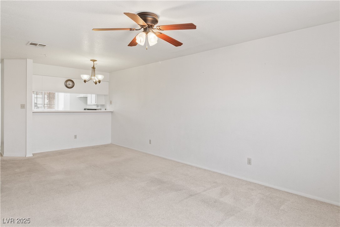 2036 Mesquite Lane, Unit 103 Laughlin, NV 89029 - Photo 15 of 67 Unfurnished living room featuring light carpet, ceiling fan with notable chandelier, and visible vents