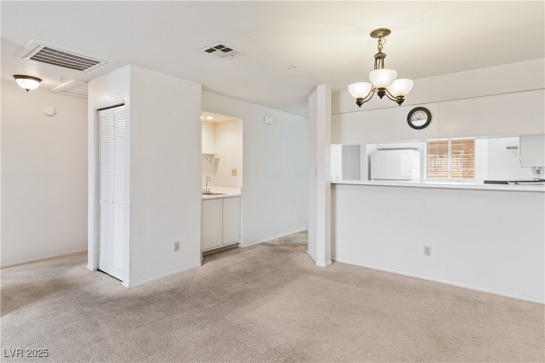 2036 Mesquite Lane, Unit 103 Laughlin, NV 89029 - Photo 17 of 67 Unfurnished living room featuring light colored carpet, visible vents, and a chandelier