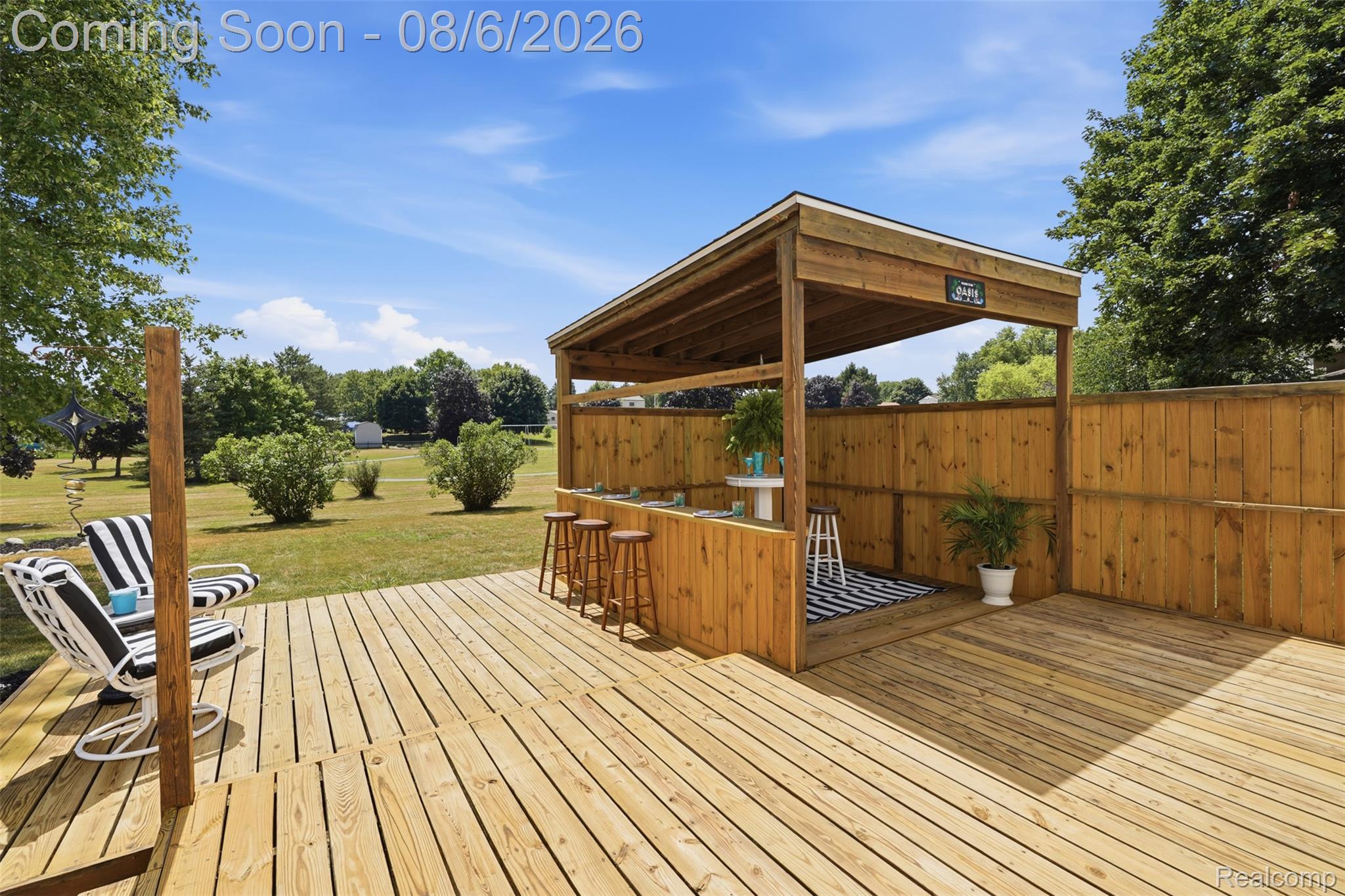 3585 Loon Lake Road Wixom, MI 48393 - Photo 28 of 40 Expansive composite deck featuring multiple wood-finish levels, a covered pavilion with full-height wood paneling and bar counter with seating, and open sightlines across manicured grounds bordered by mature landscaping