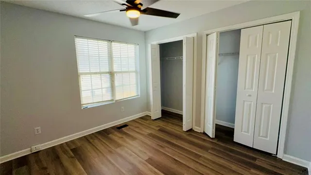 an empty room with wooden floor fan and windows
