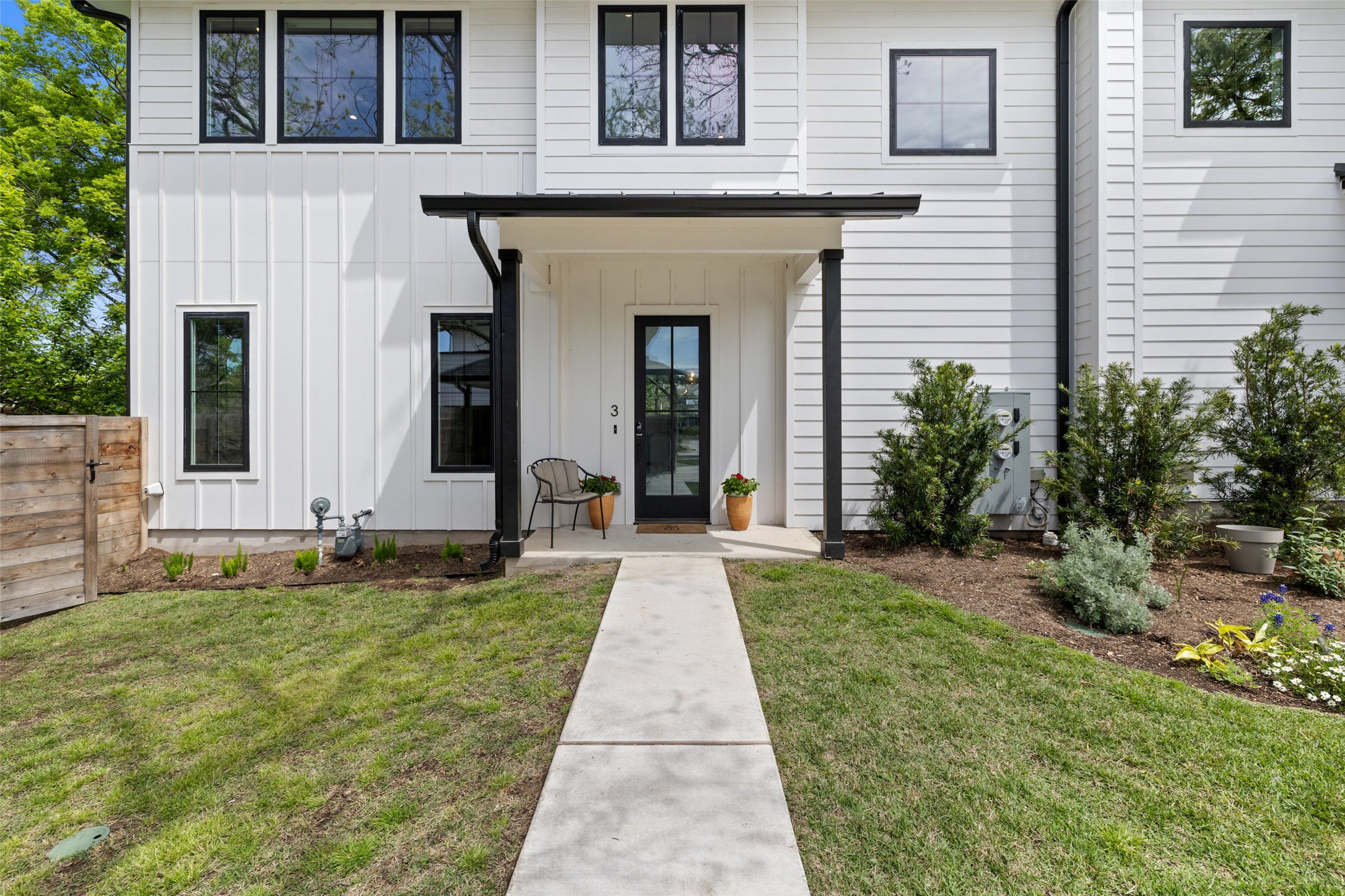 1504 Ruth Avenue, Unit 3 Austin, TX 78757 - Photo 2 of 39 A welcoming front entrance features a sleek black door and contrasting white siding, framed by youthful landscaping.