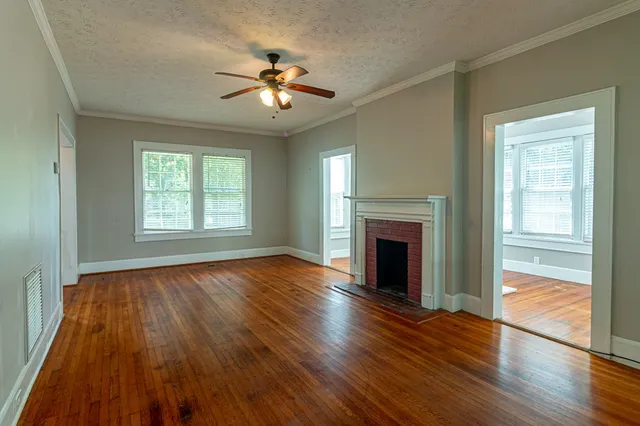 a view of an empty room with wooden floor fireplace and a window