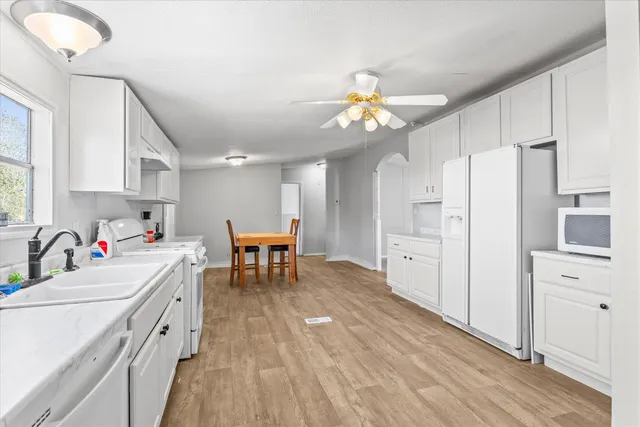 a kitchen with stainless steel appliances a refrigerator a sink dishwasher a stove and white cabinets with wooden floor