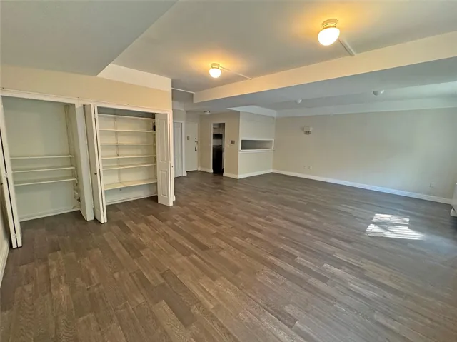 an empty room with wooden floor closet and windows